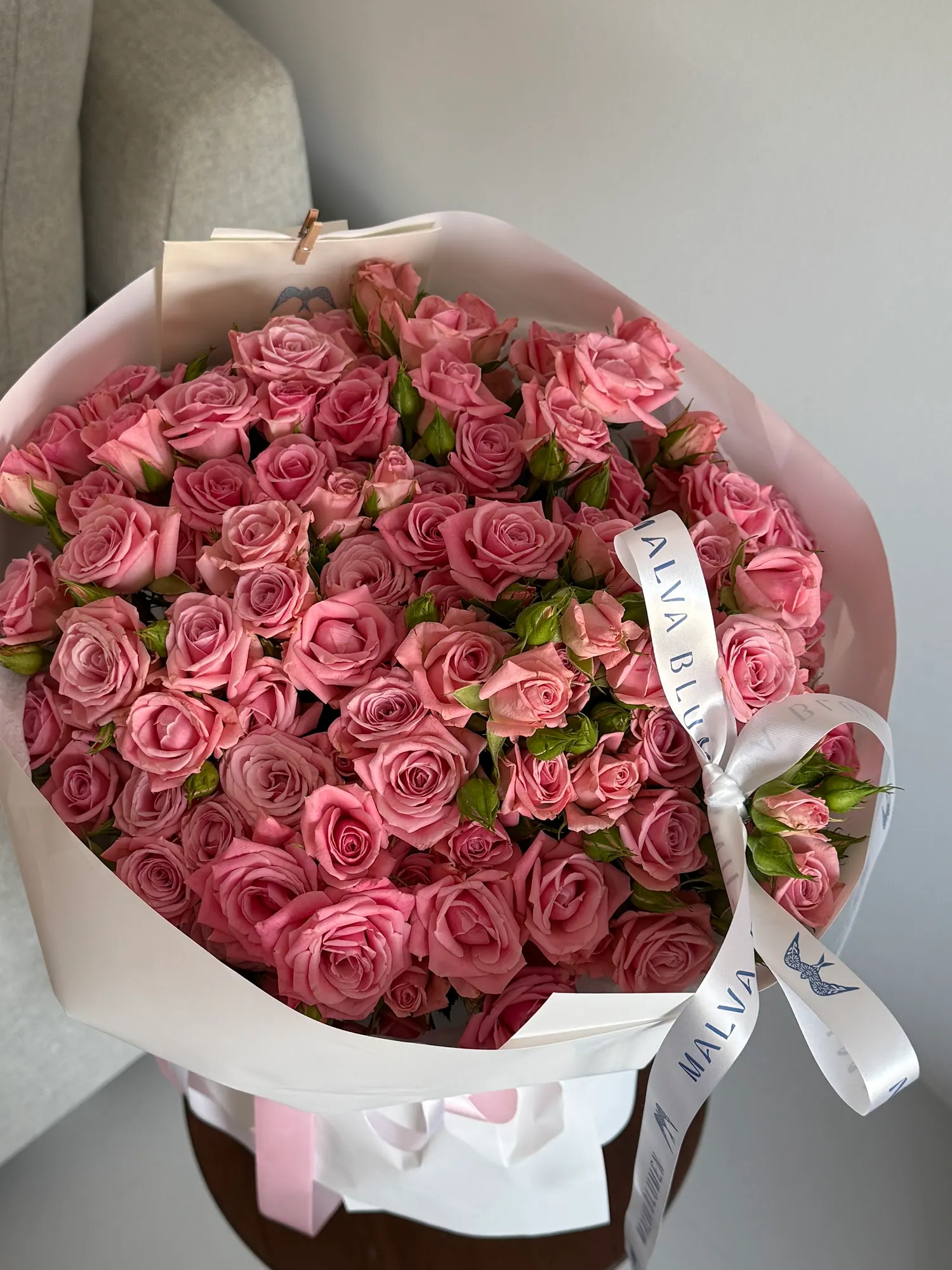 Großer Strauß aus rosa Sprayrosen in weißem Papier, gebunden mit einem Satinband mit dem Schriftzug Malva Blumen