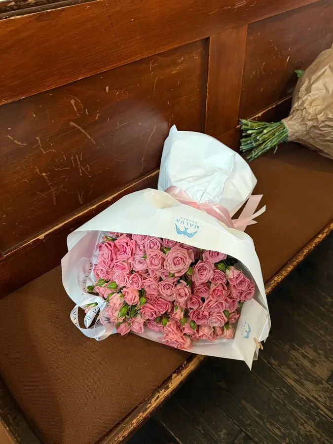 Rosa Rosenstrauß in weißem Papier auf einer Holzbank